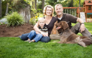 heterosexual family in a backyard. there is a lot of greenery in picture.