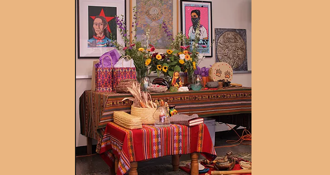 bright red and patterned table clothes over two tables, that are overflowing with flowers, bowls, gifts, woven baskets, corn and more.